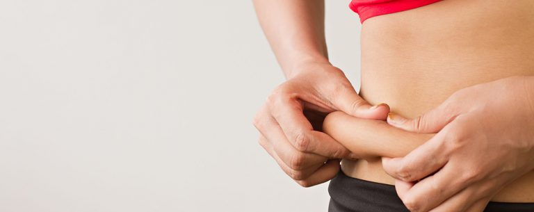 Vrouwenhand die overmatig buikvet vasthoudt