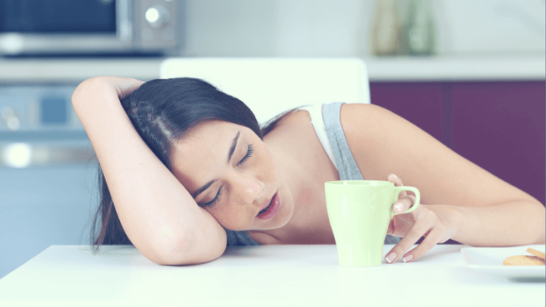 Vrouw ligt op tafel te slapen met een kopje koffie ernaast