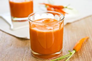 Wortelen en sinaasappelsap in een glas op houten tafel