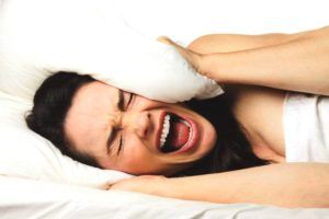Vrouw ligt schreeuwend in bed met een kussen op haar hoofd