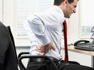 man zit achter bureau en heeft last van zijn rug